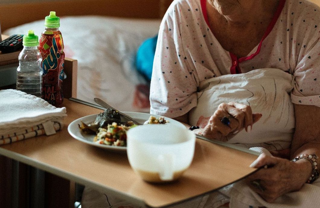 Elderly woman enjoying a meal in a cozy retirement home setting.