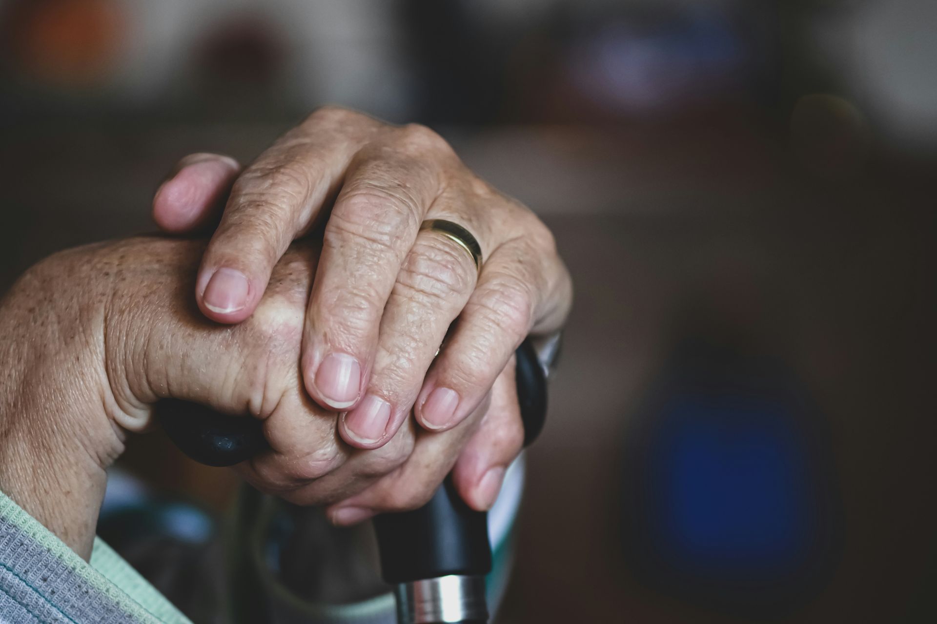 Wrinkled hands with a gold ring resting on a black cane handle